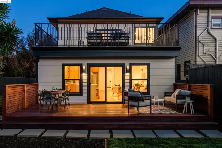 Multi-level exterior featuring a ground-level wood deck with integrated privacy screens, a second-story balcony with decorative metal railings, and a sliding glass door providing access to the interior