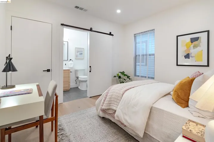 Light wood-finish flooring complements white walls, featuring a sliding barn door entry to a bathroom with a wood vanity and gray tile flooring