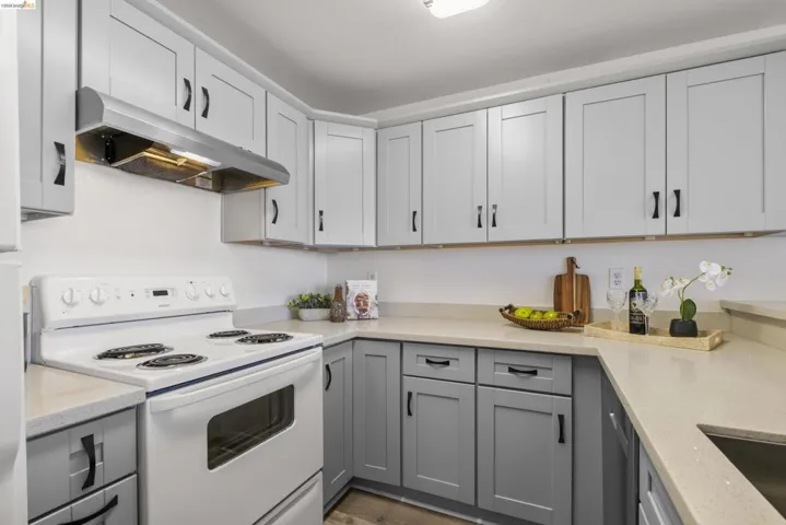 Kitchen featuring two-tone cabinetry with light upper cabinets and darker lower cabinets, light-toned countertops, a stainless steel range hood, and a white electric range