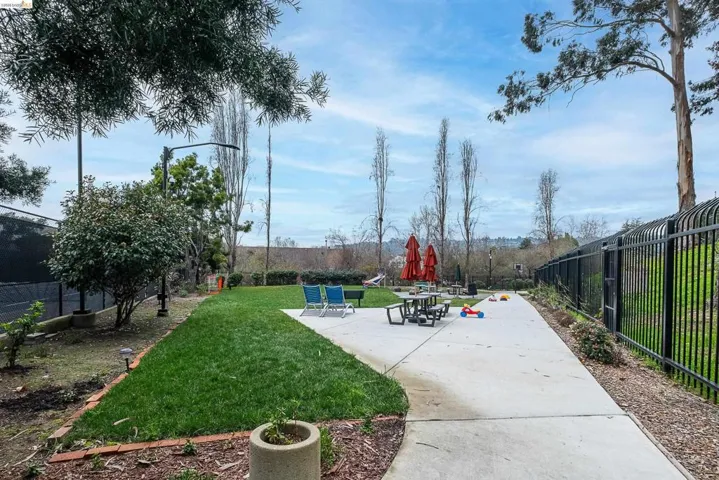 Expansive outdoor space featuring a manicured lawn, concrete patio, and a black wrought iron fence