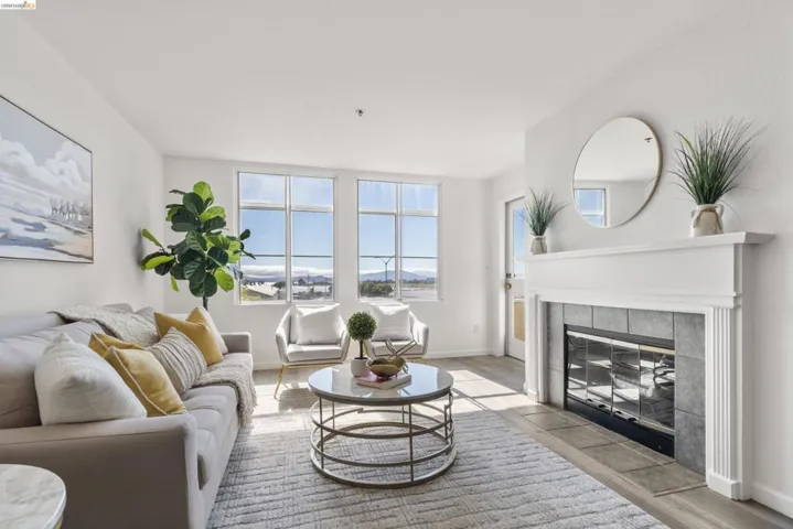 Living area featuring a white mantel fireplace with a tiled surround, wood-finish flooring, and multiple large windows with exterior visibility