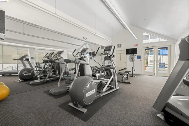 Fitness center featuring cardio equipment, strength training apparatus, mirrored wall, vaulted ceilings, and direct outdoor access