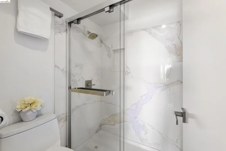 Glass-enclosed shower with large format white tile featuring grey and gold veining