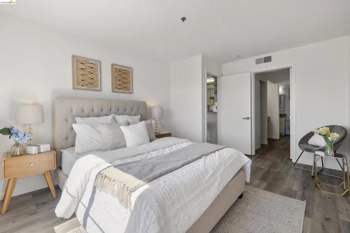 Spacious room featuring light-toned walls, wood-finish flooring, a tufted headboard, and recessed lighting