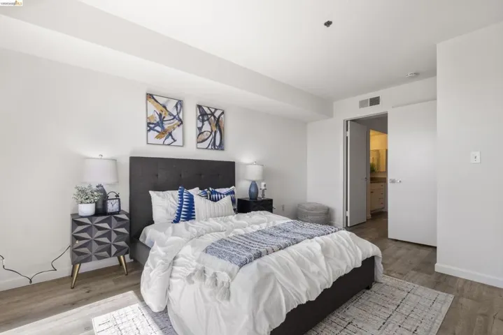 Spacious room featuring wood-finish flooring, a built-in air vent, and a doorway revealing a bathroom vanity with a mirror