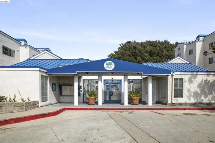 Entryway featuring a blue metal roof, white stucco exterior, prominent signage, decorative columns, and a paved approach