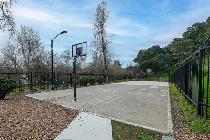 Outdoor basketball court with concrete surfacing, black perimeter fencing, and established landscaping