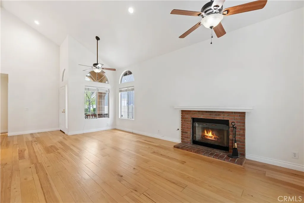 Living room with a gas brick fireplace, & a raised hearth, 2 ceiling fans & vaulted ceilings.