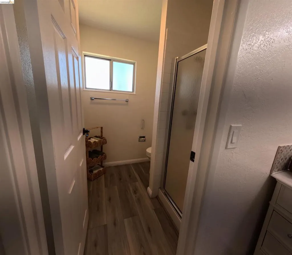 Bathroom featuring wood-finish flooring, a frosted window, and a glass-enclosed shower