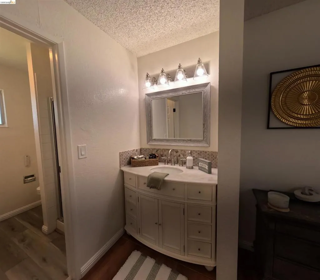 Curved vanity with a stone countertop and integrated sink, framed mirror, and a five-light fixture