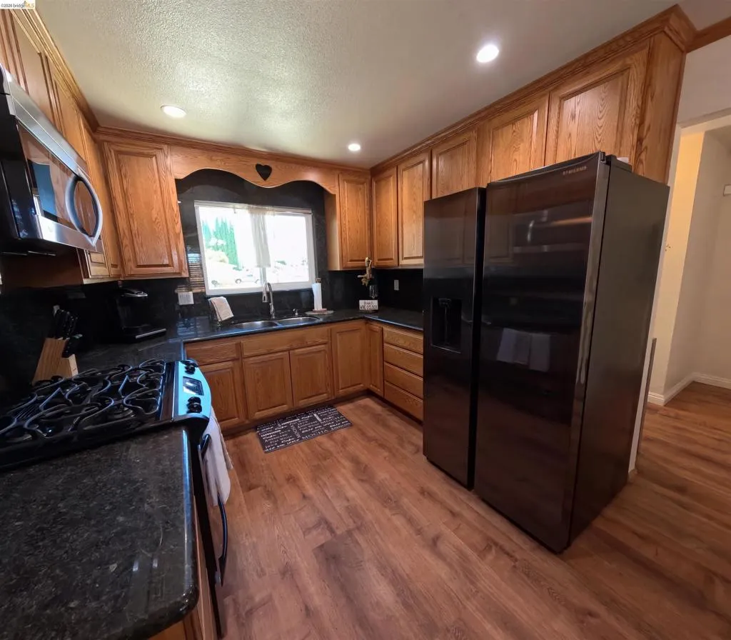 Kitchen featuring wood cabinetry, dark countertops, wood-finish flooring, recessed lighting, and a stainless steel sink