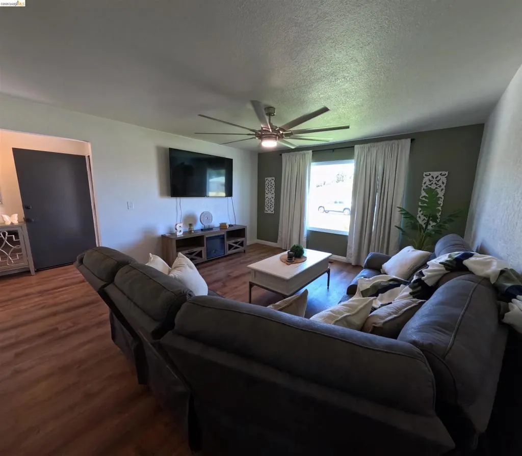 Living area featuring wood-finish flooring, a contemporary ceiling fan with integrated lighting, and a multi-tone wall palette