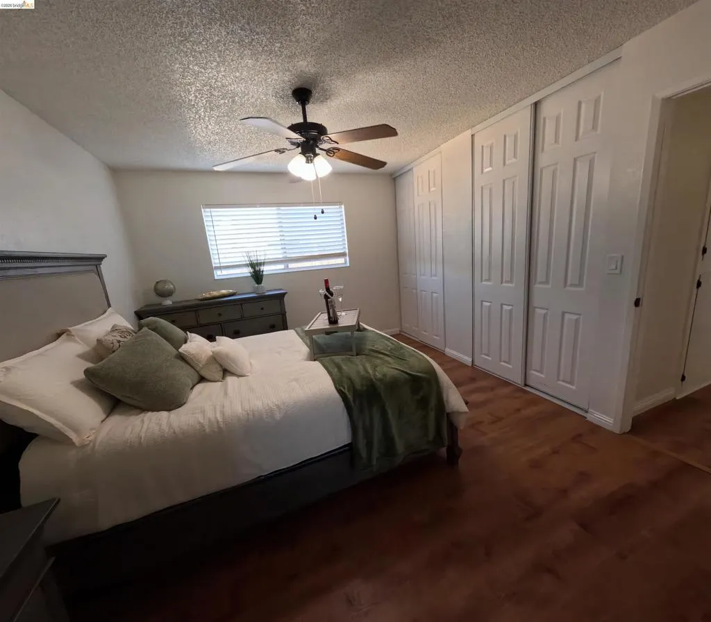 Bedroom featuring wood-finish flooring, a window with horizontal blinds, and a ceiling fan with integrated lighting