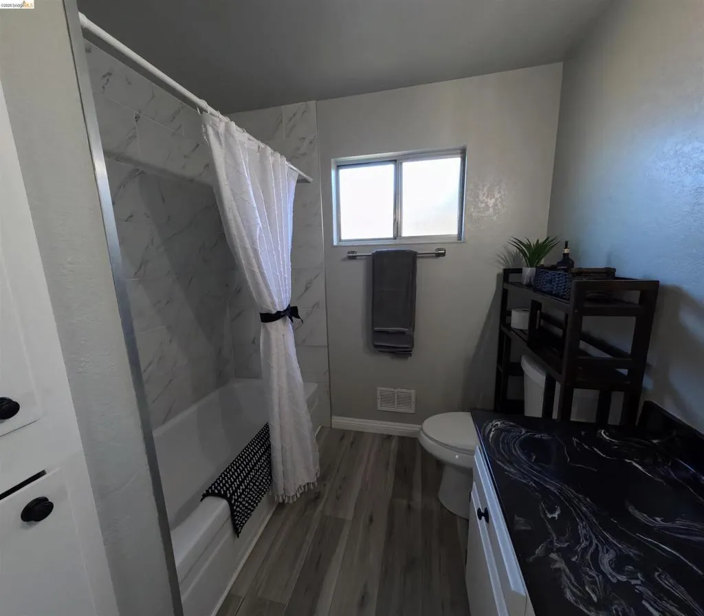 Bathroom featuring a white bathtub, marble-patterned tile shower surround, and wood-finish flooring