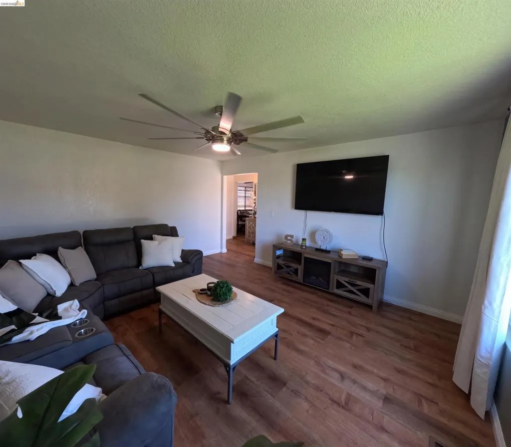 Living area with wood-finish flooring, a contemporary ceiling fan, and light-toned walls
