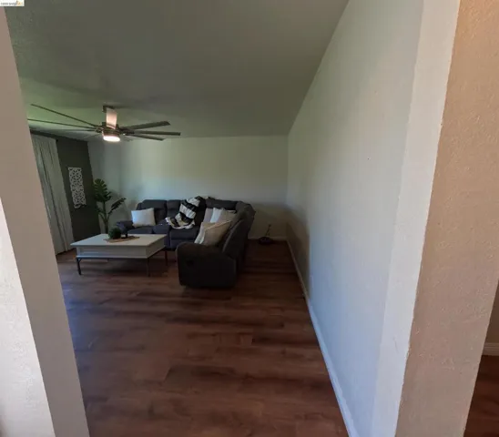 Spacious living area featuring wood-finish flooring, a contemporary ceiling fan with integrated lighting, and a neutral color palette
