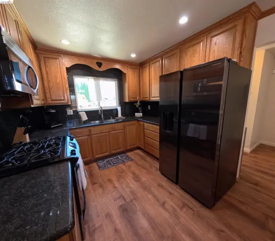 Kitchen featuring wood cabinetry, dark countertops, wood-finish flooring, recessed lighting, and a stainless steel sink