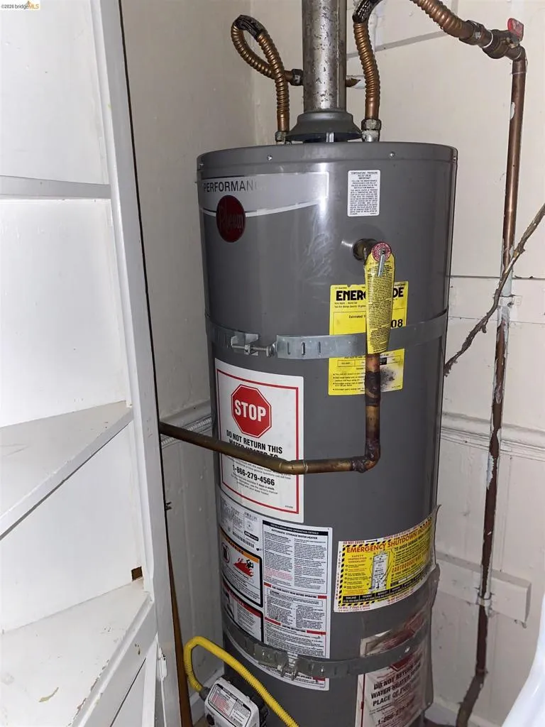 Utility closet featuring a water heater with visible piping and an adjacent built-in shelving unit