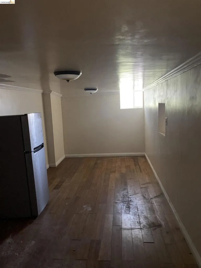 Wood-finish flooring with baseboard trim, wall-mounted light fixtures, and a compact window