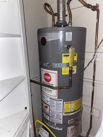 Utility closet featuring a water heater with visible piping and an adjacent built-in shelving unit