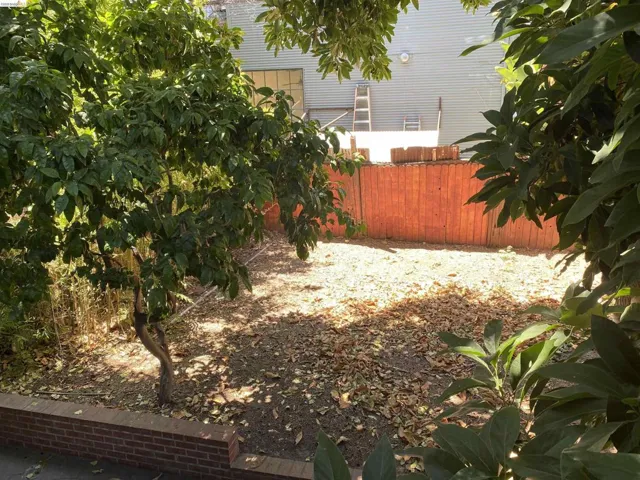 Outdoor area featuring a brick retaining wall, mature trees, and a wood fence