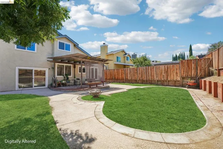 Expansive backyard featuring a central lawn area, concrete patio with decorative stone accents, and a built-in pergola