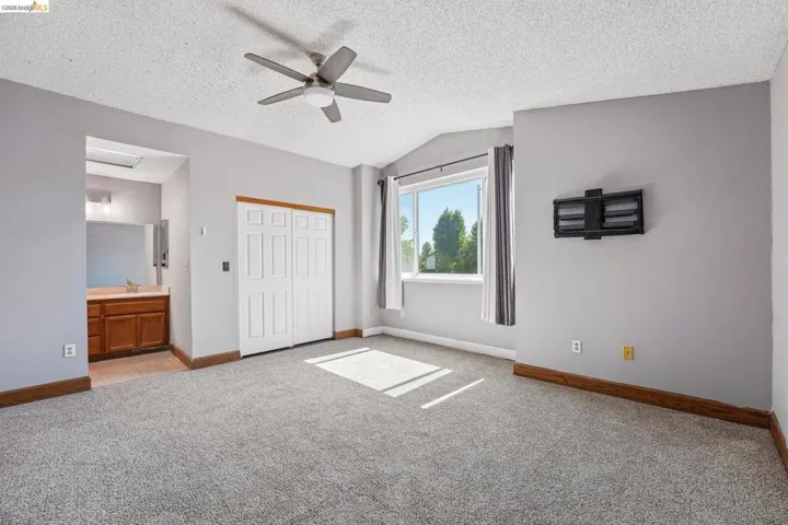 Carpeted room featuring a ceiling fan, a built-in closet with bi-fold doors, and a window with natural light