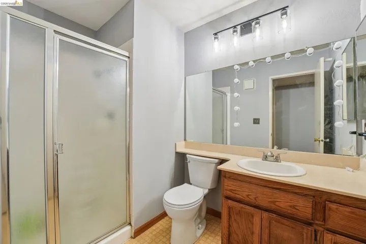 Bathroom featuring a glass-enclosed shower, wood-finish vanity with an integrated sink, a large wall-mounted mirror, and overhead track lighting