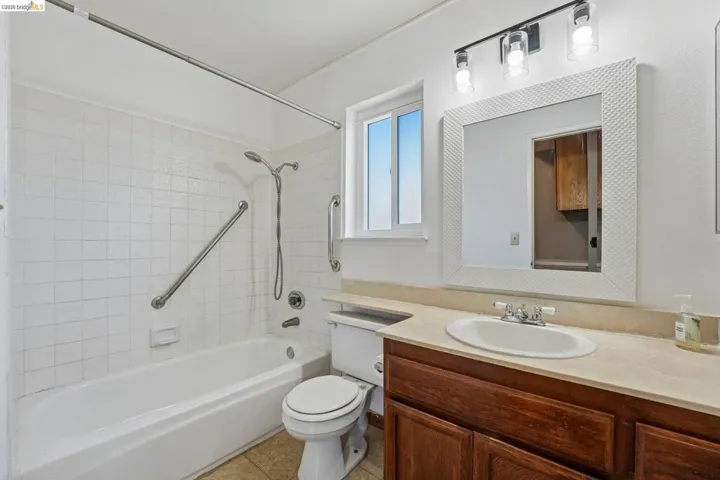 Bathroom featuring a white subway tile tub surround, a window providing natural light, a dark wood-finish vanity with an integrated sink, a light-toned countertop, and a framed mirror with overhead lighting