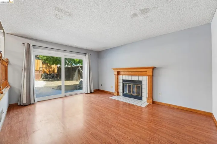 Living area featuring wood-finish flooring, a fireplace with a light wood mantel and white tile surround, and sliding glass doors