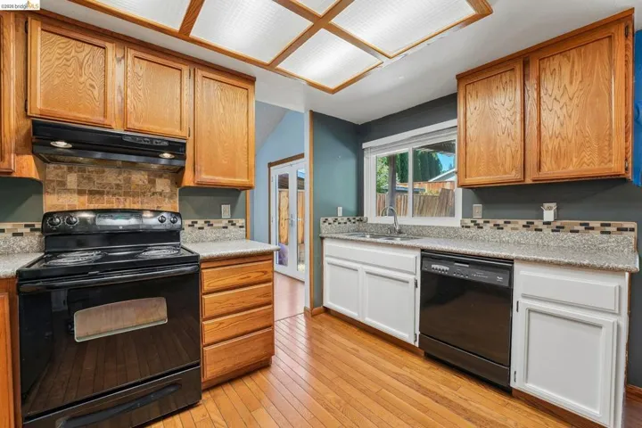 Kitchen featuring wood-finish flooring, oak cabinetry, black appliances, light-toned countertops, and a tiled backsplash