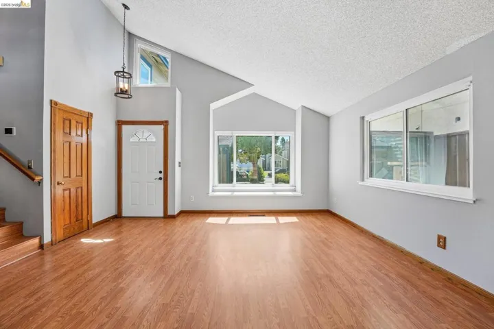 Spacious living area featuring vaulted ceilings, wood-finish flooring, and multiple windows for abundant natural light