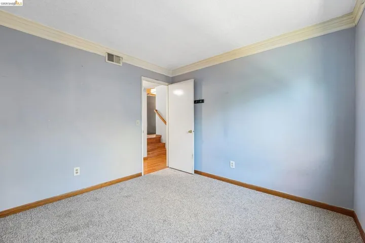 Carpeted room featuring light blue walls, white crown molding, and wood-finish baseboards