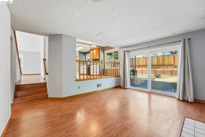 Spacious main living area featuring wood-finish flooring, a sliding glass door providing direct access to the backyard, and a stairwell with wood railings