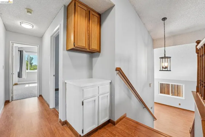Hallway featuring wood-finish flooring, built-in cabinetry with a countertop, recessed lighting, and a staircase with a wood handrail