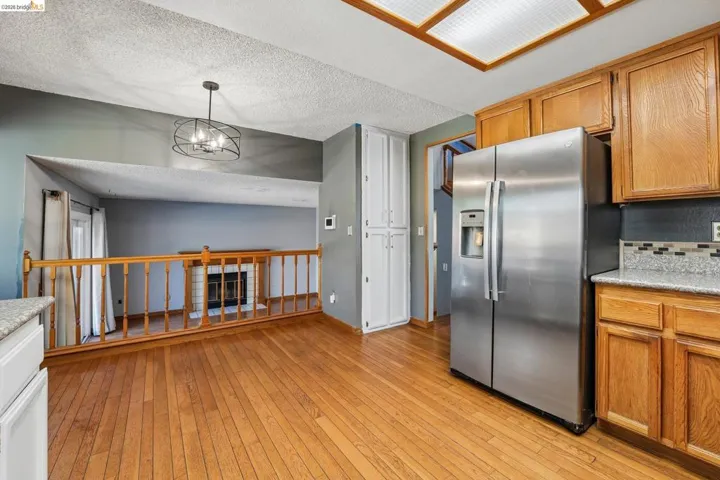 Kitchen area featuring wood-finish flooring, wood cabinetry, stainless steel refrigerator, and granite-style countertops