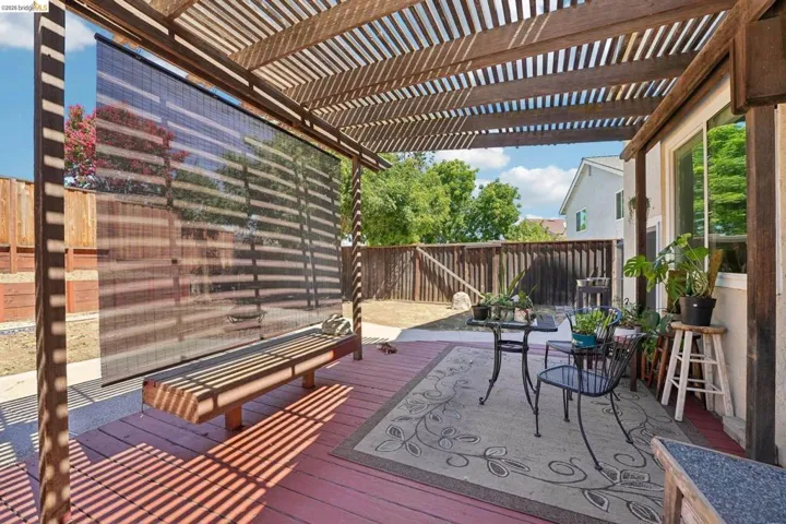 Pergola-covered patio featuring a privacy screen, wood-finish decking, and a paved outdoor area