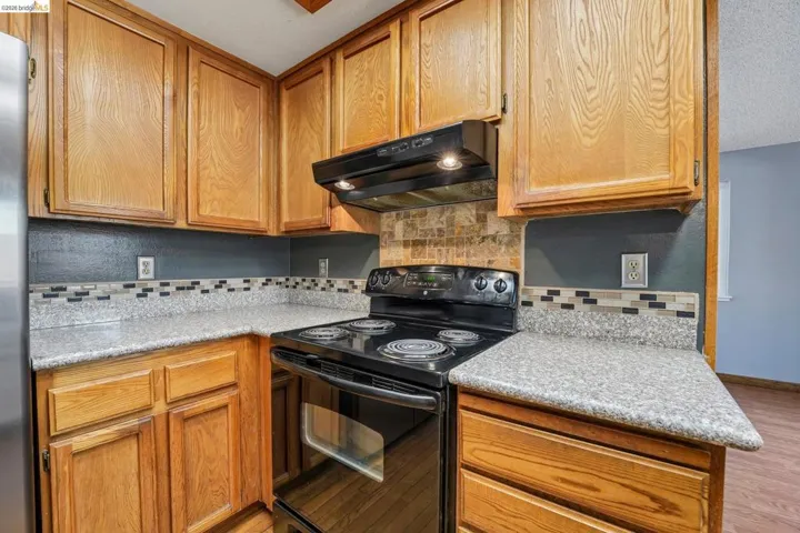 Kitchen featuring wood cabinetry, speckled countertops, and a black electric range with an overhead microwave