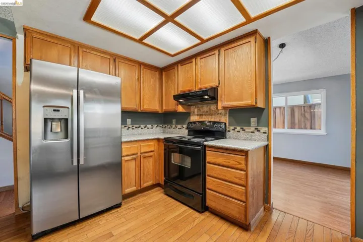 Kitchen with wood-finish flooring, warm wood cabinetry, and a stainless steel side-by-side refrigerator