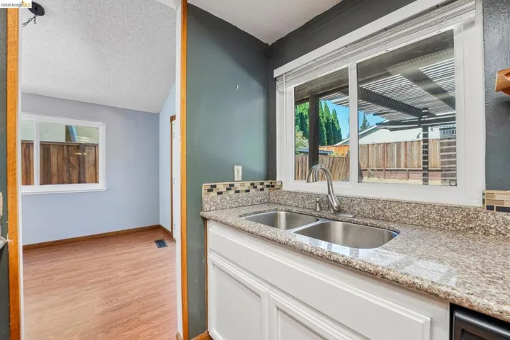 Kitchen sink area featuring a double-basin stainless steel sink, granite-style countertops, white cabinetry, and a mosaic tile backsplash