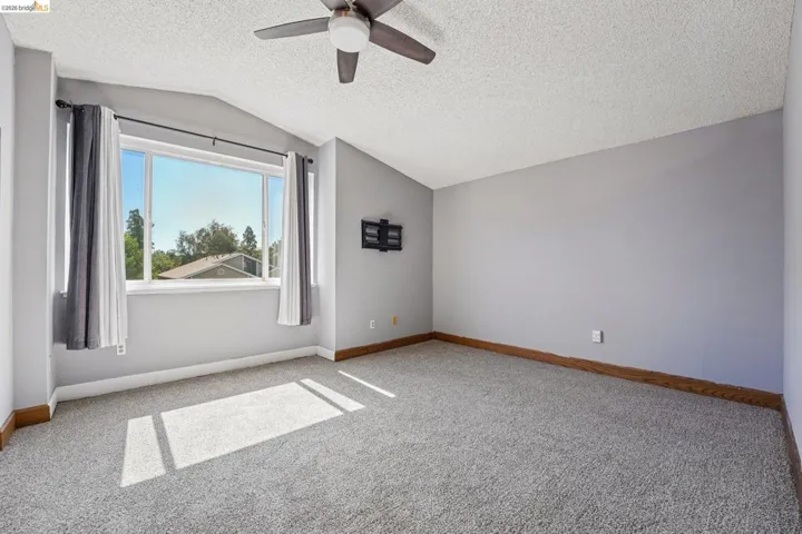Spacious room featuring vaulted ceilings, a ceiling fan, plush gray carpeting, and a large multi-pane window