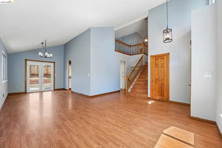 Vaulted ceilings enhance the main living area, featuring wood-finish flooring throughout, a chandelier, and French doors leading to the exterior