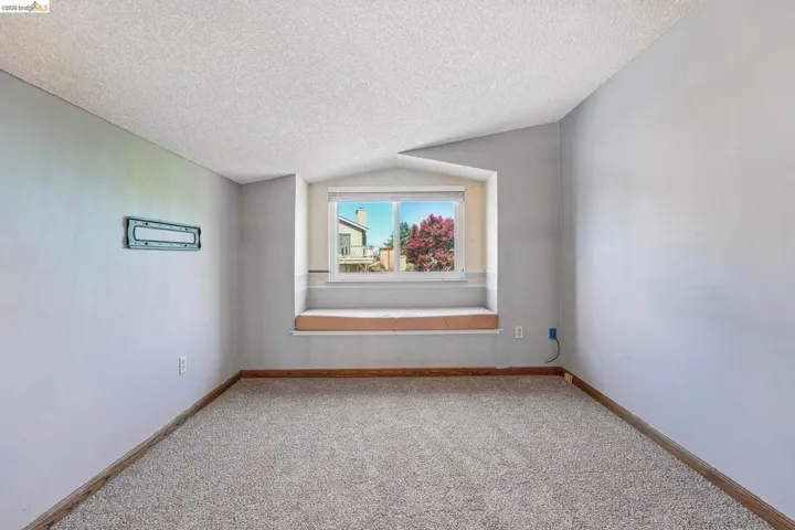Room featuring a built-in window seat, a framed window, light gray carpeting, and a wall-mounted bracket