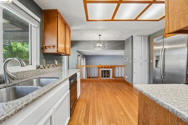Kitchen featuring wood-finish flooring, wood cabinetry, granite-style countertops, and a dual-basin stainless steel sink with a gooseneck faucet