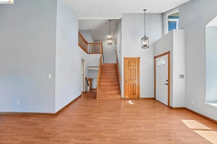 Entryway featuring wood-finish flooring, a prominent wooden staircase with matching railings, high ceilings, and two suspended lantern-style light fixtures