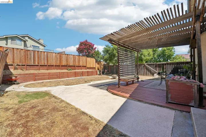 Expansive backyard with a wooden pergola, concrete patio, multi-level wooden fencing, and a terraced garden area