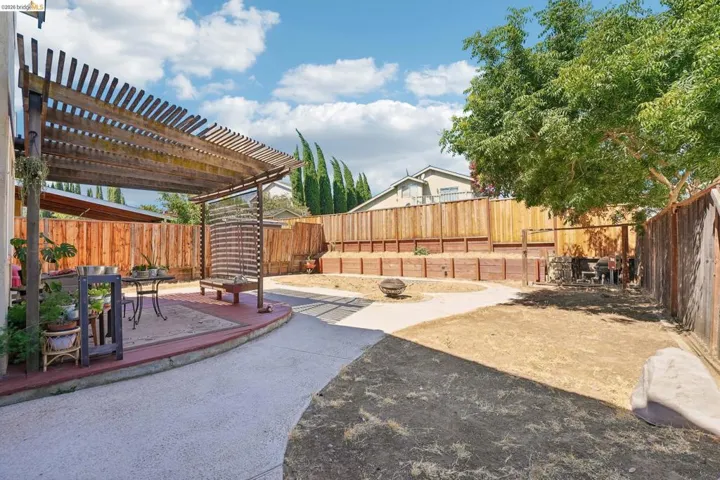 Expansive backyard featuring a wood pergola over a curved concrete patio, a distinct concrete pathway, mature trees, and a terraced retaining wall system