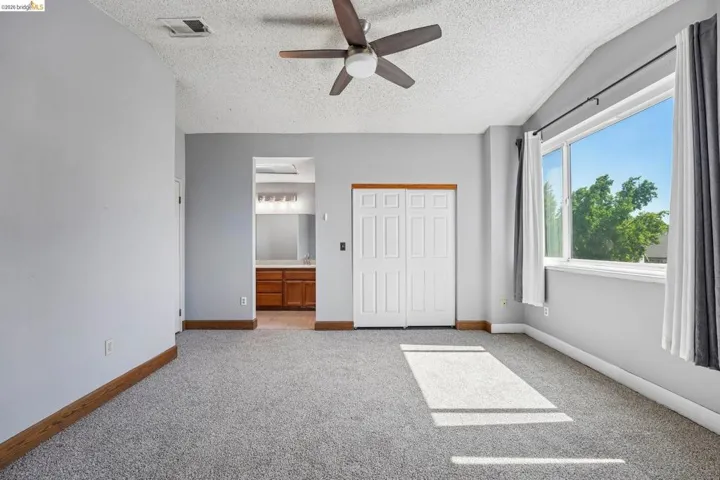 Carpeted room featuring a ceiling fan, a large window, bi-fold closet doors, and wood-finish baseboards