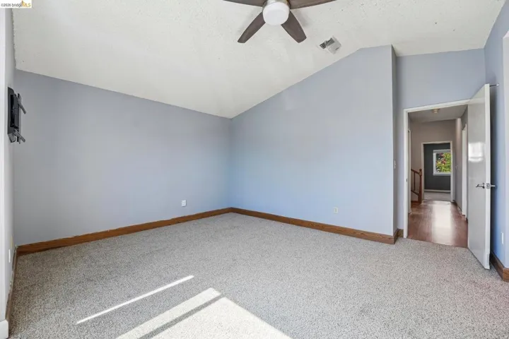 Spacious room featuring vaulted ceilings, a ceiling fan with integrated lighting, light-colored carpeting, and a wood-finish baseboard trim
