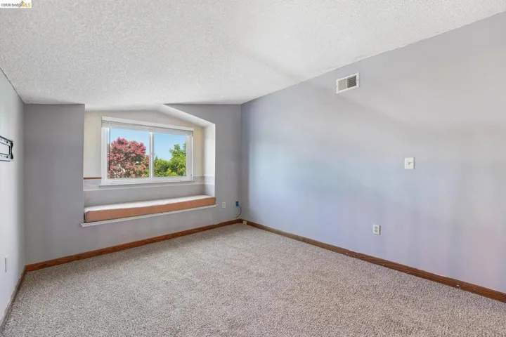 Recessed window alcove with a built-in bench, neutral carpeting, light gray wall paint, white trim, and a textured ceiling